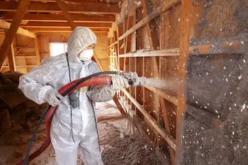 A worker dressed in protective gear spraying the walls of an attic space with insulation as part of Griffin Pest Solutions’ attic insulation services.